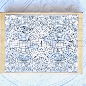 Puede incluir: Un sello de madera con un dise&ntilde;o vintage que presenta dos mapas del mundo, una br&uacute;jula y detalles florales. Los mapas est&aacute;n delineados en negro y tienen un patr&oacute;n de cuadr&iacute;cula.