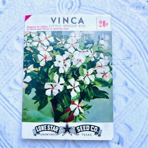 May include: Vintage seed packet for Vinca Little Bright Eye flowers. The packet features a colorful illustration of white flowers with red centers and green leaves. The text reads "Famous for ability to thrive and bloom in extreme heat."