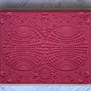 Puede incluir: Un sello de goma rojo con un dise&ntilde;o detallado que presenta dos c&iacute;rculos superpuestos con un patr&oacute;n de cuadr&iacute;cula y intrincados detalles florales alrededor de los bordes.