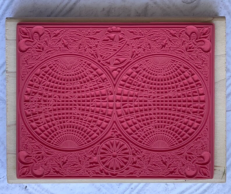 Puede incluir: Un sello de goma rojo con un dise&ntilde;o detallado que presenta dos c&iacute;rculos superpuestos con un patr&oacute;n de cuadr&iacute;cula y intrincados detalles florales alrededor de los bordes.