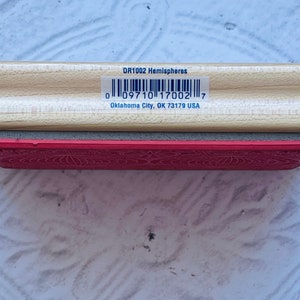 Puede incluir: Un sello de madera con una almohadilla de goma roja. El sello est&aacute; etiquetado como "DR1002 Hemispheres" y tiene un c&oacute;digo de barras con el n&uacute;mero "0 09710 17002 7". El texto "Oklahoma City, OK 73179 USA" tambi&eacute;n est&aacute; impreso en el sello.