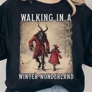 May include: Black sweatshirt featuring a winter scene with a horned figure in a red coat and a girl in a red dress, walking in a snowy forest. The text "WALKING IN A WINTER WONDERLAND" is printed above and below the image.