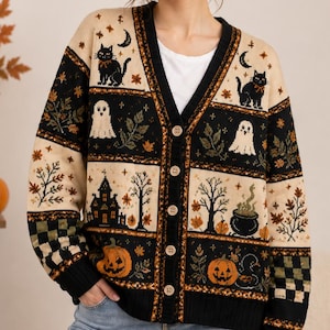 May include: A beige and black button-down cardigan featuring a repeating Halloween-themed pattern. The knit design includes black cats, white ghosts, haunted houses, bubbling cauldrons, orange jack-o'-lanterns, bare trees, and checkered accents.