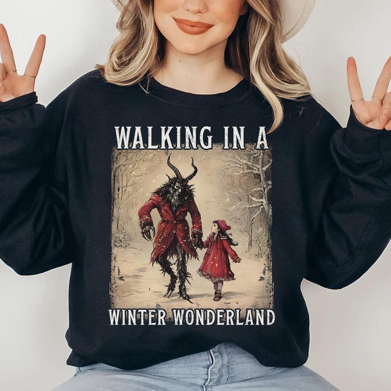 May include: Black sweatshirt featuring a winter scene with a horned figure in a red coat and a girl in a red dress, walking in a snowy forest. The text "WALKING IN A WINTER WONDERLAND" is printed above and below the image.