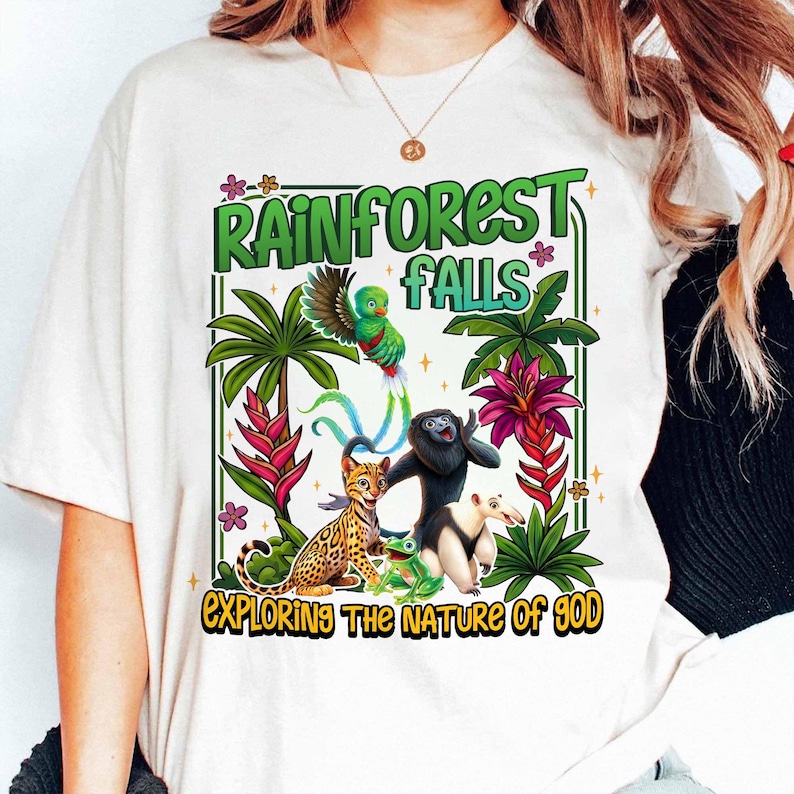 May include: White t-shirt with a colorful rainforest graphic. The design features a green parrot, a black monkey, a spotted cat, a frog, and an anteater, with the text "RAINFOREST FALLS" and "EXPLORING THE NATURE OF GOD".