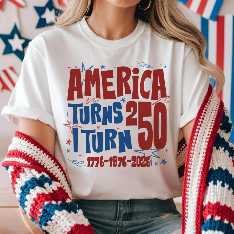 May include: White t-shirt with the text "AMERICA TURNS 250 I TURN 50 1776-1976-2026" in red and blue. The shirt is worn with a red, white, and blue patterned sweater.