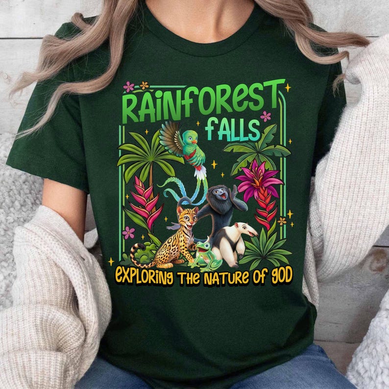 May include: Dark green t-shirt with a colorful rainforest graphic. The design includes a parrot, jaguar, frog, and other animals, along with the text "RAINFOREST FALLS EXPLORING THE NATURE OF GOD".
