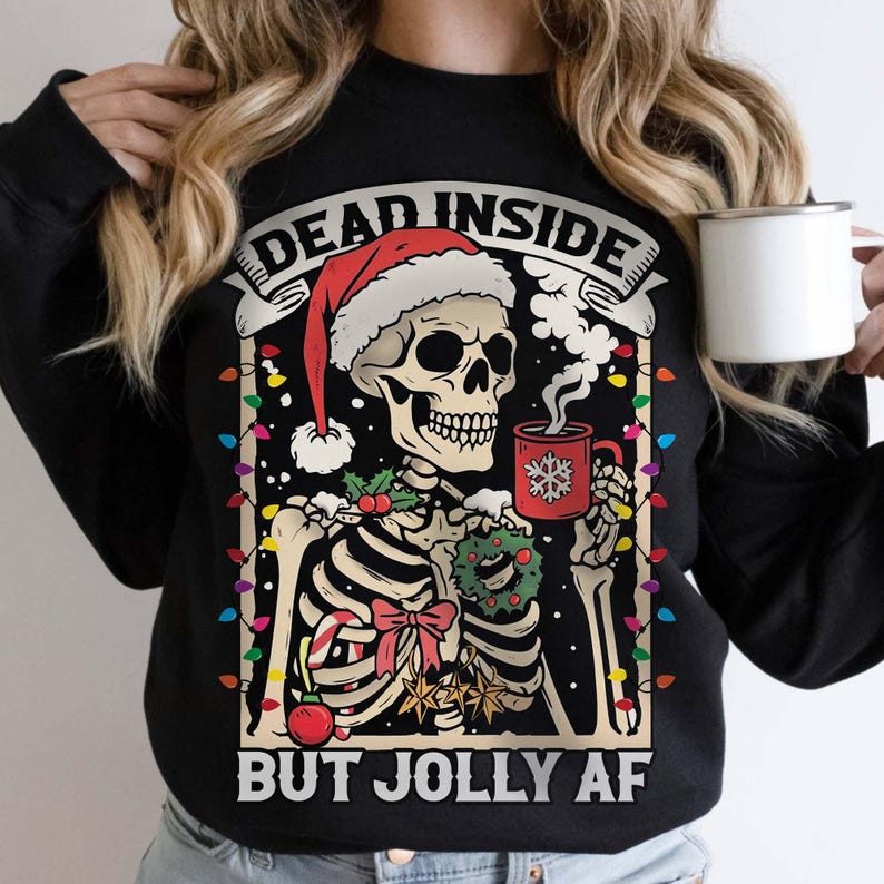May include: Black Christmas sweater with a skeleton wearing a Santa hat and holding a mug of hot cocoa. The sweater has the text "Dead Inside But Jolly AF" printed on it.