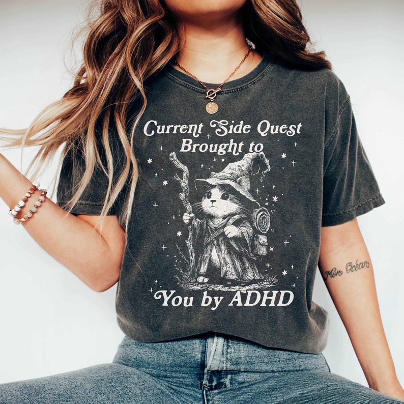 Celebrate neurodivergent humor with this Current Side Quest Brought to You by ADHD graphic t-shirt. This shirt is made for those who embrace mental health awareness, side quests, and a sense of humor about everyday distractions. Ideal for ADHDers, gamers, RPG lovers, and anyone who lives life one side quest at a time.