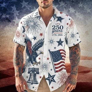 May include: White button-down shirt with a patriotic design. Features an American flag, an eagle, fireworks, stars, and the text "250 years 1776-2026". The shirt has short sleeves and a classic collar.