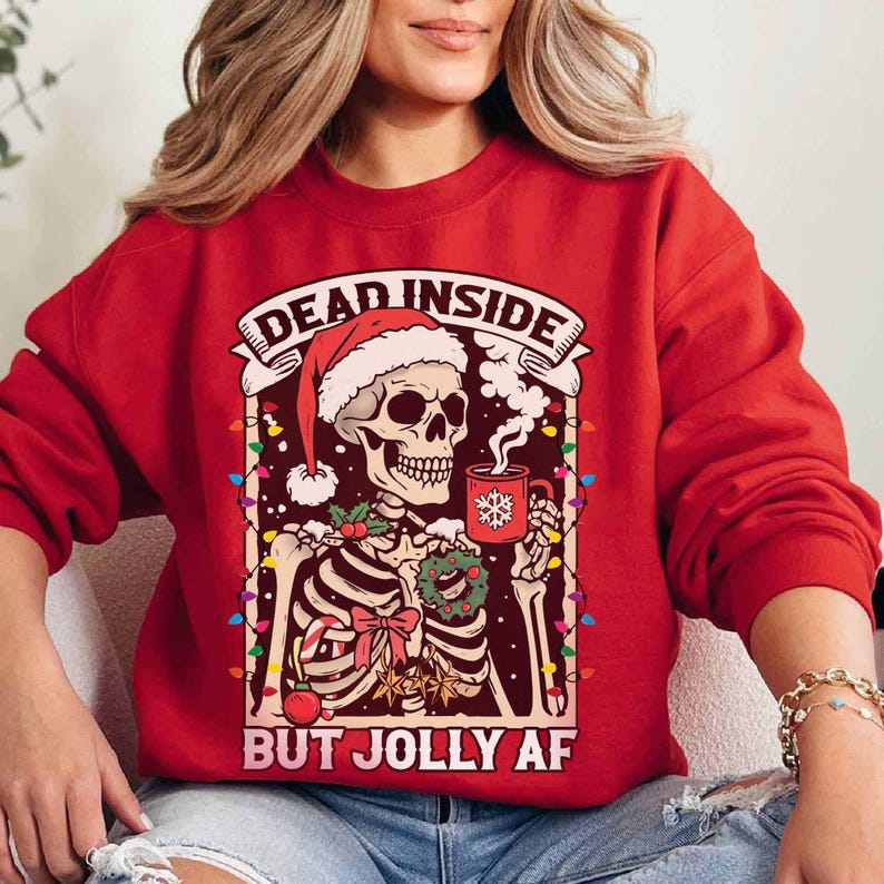 May include: Red Christmas sweater with a skeleton wearing a Santa hat and holding a mug of hot cocoa. The sweater has the text "Dead Inside But Jolly AF" printed on it.