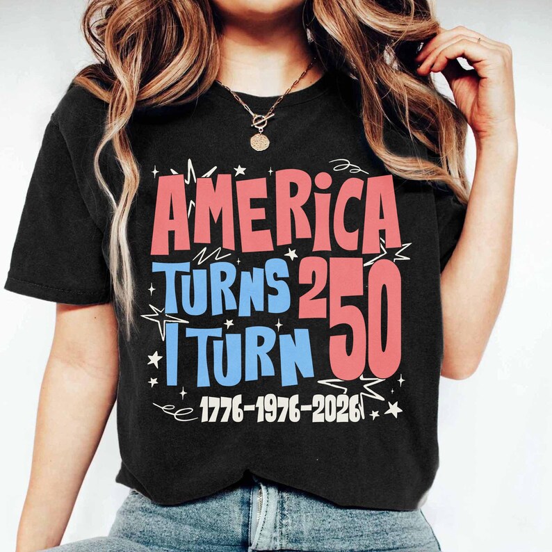 May include: Black t-shirt with the text "AMERICA TURNS 250 I TURN 50" in red and blue, with the years 1776-1976-2026 in white. The shirt has a crew neck and short sleeves.