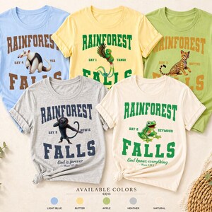 May include: Five colorful t-shirts with rainforest-themed designs. Each shirt features the text "Rainforest Falls" with a different animal illustration and the words "Day" and a name. Available in light blue, butter, apple, heather, and natural.