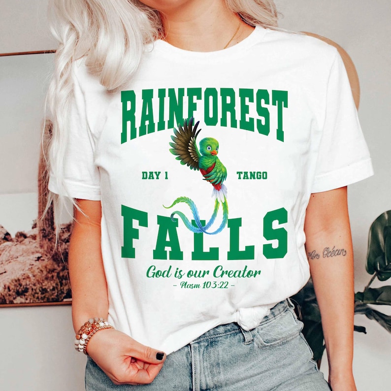 May include: White t-shirt with a green graphic that reads "RAINFOREST FALLS" with a colorful bird illustration. The text "God is our Creator - Psalm 103:22" is also printed on the shirt.
