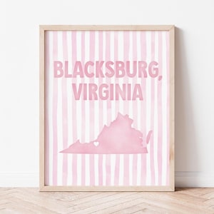 May include: A framed wall art print featuring the text Blacksburg, Virginia in pink letters over a light pink and white vertical striped background, with a pink silhouette map of Virginia containing a small white heart over Blacksburg.