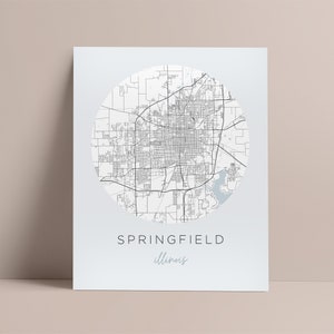 Puede incluir: Un mapa en blanco y negro de Springfield, Illinois, en un círculo sobre un fondo azul claro. El texto "SPRINGFIELD" e "Illinois" está debajo del mapa.