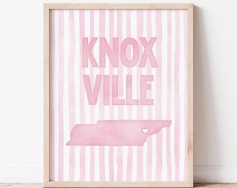 Può includere: Una stampa artistica incorniciata con uno sfondo a righe verticali rosa chiaro e bianco. Il testo KNOX VILLE è stampato in grandi lettere in grassetto rosa chiaro. Sotto il testo c'è una sagoma rosa chiaro del Tennessee con un piccolo cuore bianco.