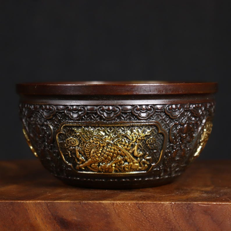 May include: A dark brown bowl with intricate gold detailing. The bowl is decorated with a dragon design and a geometric pattern.