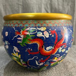 Peut inclure: Un bol décoratif bleu avec un bord doré et un motif de dragon détaillé. Le bol présente un dragon rouge et vert vibrant, des nuages et des motifs floraux. Un objet de décoration intérieure unique.