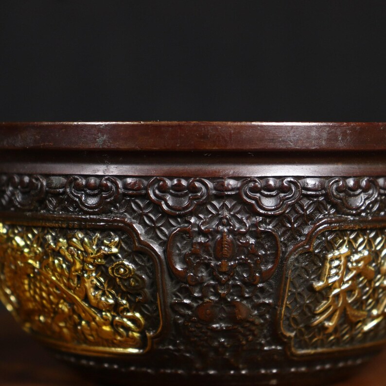 May include: A dark brown bowl with intricate carvings and gold accents. The bowl has a raised rim and a decorative pattern around the top edge.