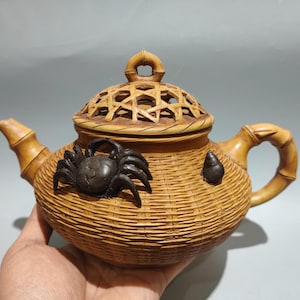 以下が含まれることがあります： 織りバスケットのデザインの装飾的なティーポット。 ティーポットはタン色で、竹スタイルのハンドルと注ぎ口が付いています。 ダークブラウンのカニが側面に付いています。 蓋は格子デザインです。