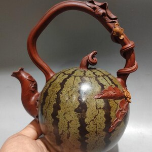 May include: A handcrafted teapot shaped like a watermelon, featuring a green and brown striped body. The handle and spout are a rich brown, with carved leaf and vine details. A unique decorative item.