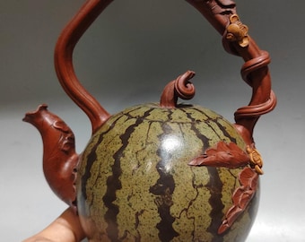 May include: A handcrafted teapot shaped like a watermelon, featuring a green and brown striped body. The handle and spout are a rich brown, with carved leaf and vine details. A unique decorative item.