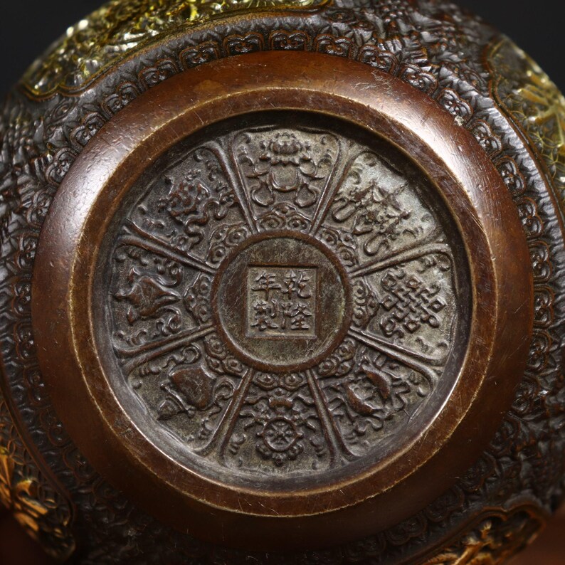 May include: A circular bronze bowl with intricate carvings and a central square with Chinese characters. The bowl is decorated with eight symbols around the edge.