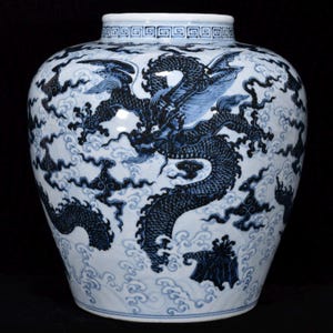 Könnte beinhalten: Ein blau-weißes Porzellangefäß mit einem detaillierten, dunkelblauen Drachenmotiv, das sich durch stilisierte Wolken und Wellen windet. Der Hals des Gefäßes ist mit einem geometrischen Mäanderband verziert und hebt sich vom weißen Untergrund ab.