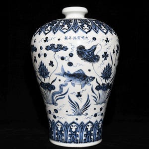 Op de afbeelding: Een witte porseleinen vaas met een blauw en wit ontwerp. De vaas is versierd met een vis, lotusbloemen en andere bloemmotieven. De vaas heeft een rond lichaam en een smalle hals. De vaas is ongeveer 30 cm hoog.
