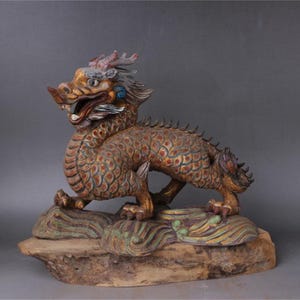 May include: A detailed, hand-carved wooden dragon statue with gold and blue paint accents. The dragon is perched on a wooden base with a swirling, painted design.