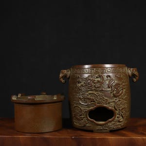 Puede incluir: Un quemador de incienso de bronce con intrincados tallados de dragones y nubes. El quemador tiene dos asas y una parte superior extra&iacute;ble.