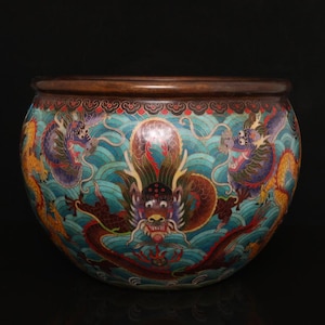 Peut inclure: Un bol cloisonné rond présentant un fond turquoise vif avec des motifs de vagues stylisés. L'extérieur est décoré de plusieurs dragons colorés dans des tons de rouge, jaune et violet, et un bord brun foncé entoure le haut du bol.