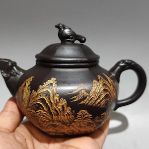 以下が含まれることがあります： 鳥の形をした蓋の取っ手と金色の風景デザインが付いた、濃い茶色のセラミックティーポット。 ティーポットは、湾曲したハンドルと注ぎ口を備えています。