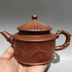 以下が含まれることがあります： 蓋と取っ手が付いた茶色のセラミックティーポット。 ティーポットは花の模様と竹風の注ぎ口が特徴です。 ハンドルは湾曲しており、蓋にはリブ模様があります。