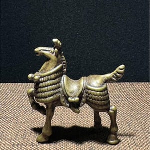 May include: A small, bronze horse figurine with a saddle and intricate details. The horse is standing on all four legs and has a raised head.
