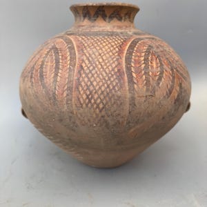May include: A brown ceramic pot with a geometric design. The pot has a rounded body and a narrow neck. The design is made up of lines and triangles.