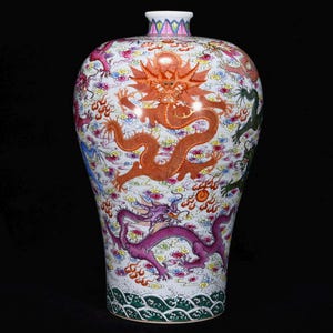 May include: A white ceramic vase with a flared top and a wide body. The vase is decorated with colorful dragons, clouds, and other traditional Chinese motifs. The dragons are in shades of red, purple, green, and blue. The vase has a green and white wave pattern at the base.