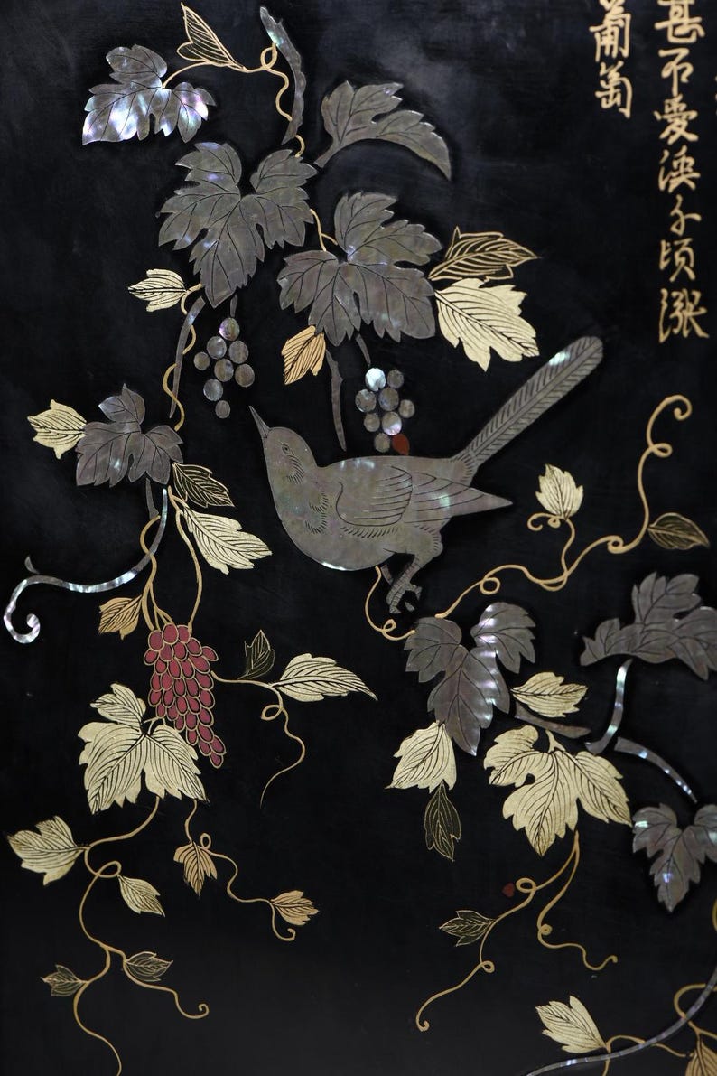 May include: A black panel featuring an inlaid design of a bird perched among grapevines. The artwork uses iridescent mother-of-pearl for the bird and leaves, with red accents for the grapes and gold-colored line work. Chinese characters appear in the top right corner.