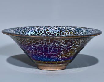 Könnte beinhalten: Eine Keramikschale mit einem Craquelé-Glasurmuster. Die Außenseite der Schale geht von Dunkelbraun in tiefes Lila und Blau über, mit einem Netzwerk aus weißen Linien. Der Rand ist dunkelbraun und der Boden hellbraun.