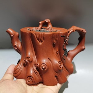 以下が含まれることがあります： 赤茶色のセラミックティーポット。切り株を模した彫刻が施されています。木の枝を模した取っ手と注ぎ口があり、節や樹皮の質感など、細部までこだわっています。蓋にも枝のような取っ手がついています。高さは約15cmです。