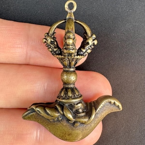 May include: A bronze-colored pendant with intricate details. The pendant features a central column with a decorative base and a loop at the top. Two dragon-like figures flank the top. The bottom has a curved, ornate design.