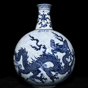 Op de afbeelding: Een blauw-witte keramische vaas met een drakenontwerp. De vaas heeft een ronde body en een lange hals. De draak is afgebeeld in blauw, met ingewikkelde details. De achtergrond heeft een golfpatroon.
