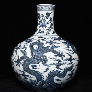 Op de afbeelding: Een grote, witte keramische vaas met een blauw drakenontwerp. De vaas heeft een bolvormige body en een lange hals met bloemmotieven. De draak is gedetailleerd en gestileerd afgebeeld. De vaas is een decoratief item, ongeveer 30 cm hoog.