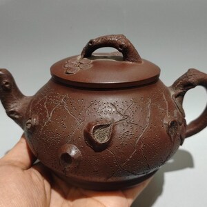 May include: A brown ceramic teapot with a lid and handle. The teapot has a textured surface with leaf and branch details. The spout and handle are curved. The teapot is a traditional style.