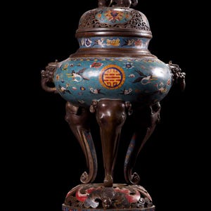 Puede incluir: Un quemador de incienso de cloisonné antiguo y ornamentado con un cuerpo turquesa, decorado con pájaros y motivos florales. El quemador tiene una base y patas de bronce, y una tapa detallada con una pequeña estatua en la parte superior. La base también está decorada con patrones coloridos.