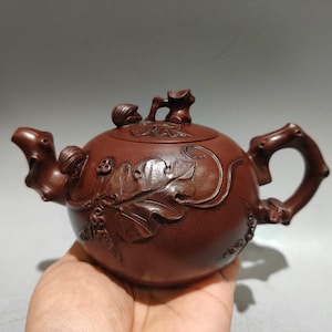 以下が含まれることがあります： 茶色のセラミックティーポット。花と葉の複雑な彫刻が施されています。 ティーポットは、湾曲したハンドル、注ぎ口、小さなノブ付きの蓋を備えています。 デザインには、詳細なレリーフワークが含まれています。