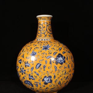 Può includere: Vaso in ceramica gialla con corpo rotondo e collo stretto. Il vaso è decorato con motivi floreali blu e volute. Il bordo è bianco. Il vaso presenta caratteri cinesi.