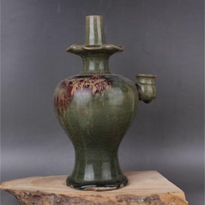 May include: A green glazed ceramic vase with a spout and a flared top. The vase has a brown and red glaze pattern.