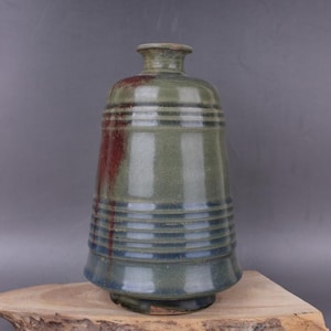 May include: A ceramic vase with a green and blue glaze. The vase has a wide base and a narrow neck. It is decorated with horizontal lines.